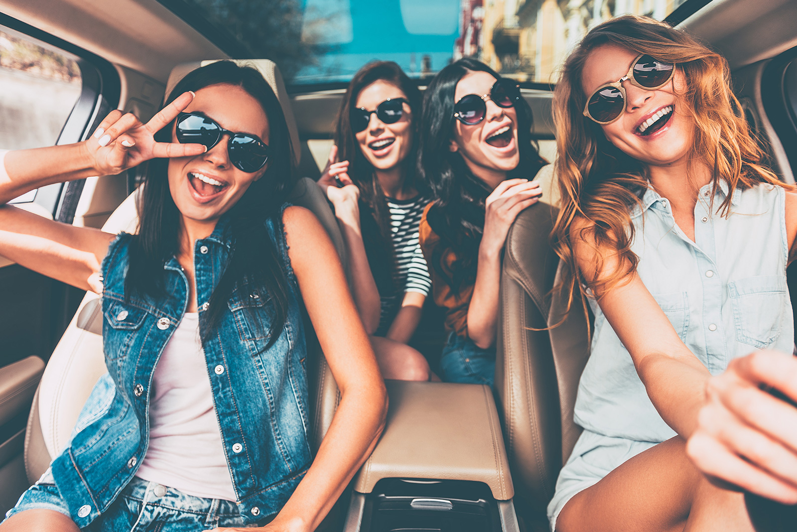 Four young women wearing sunglasses laughing together inside a vehicle.