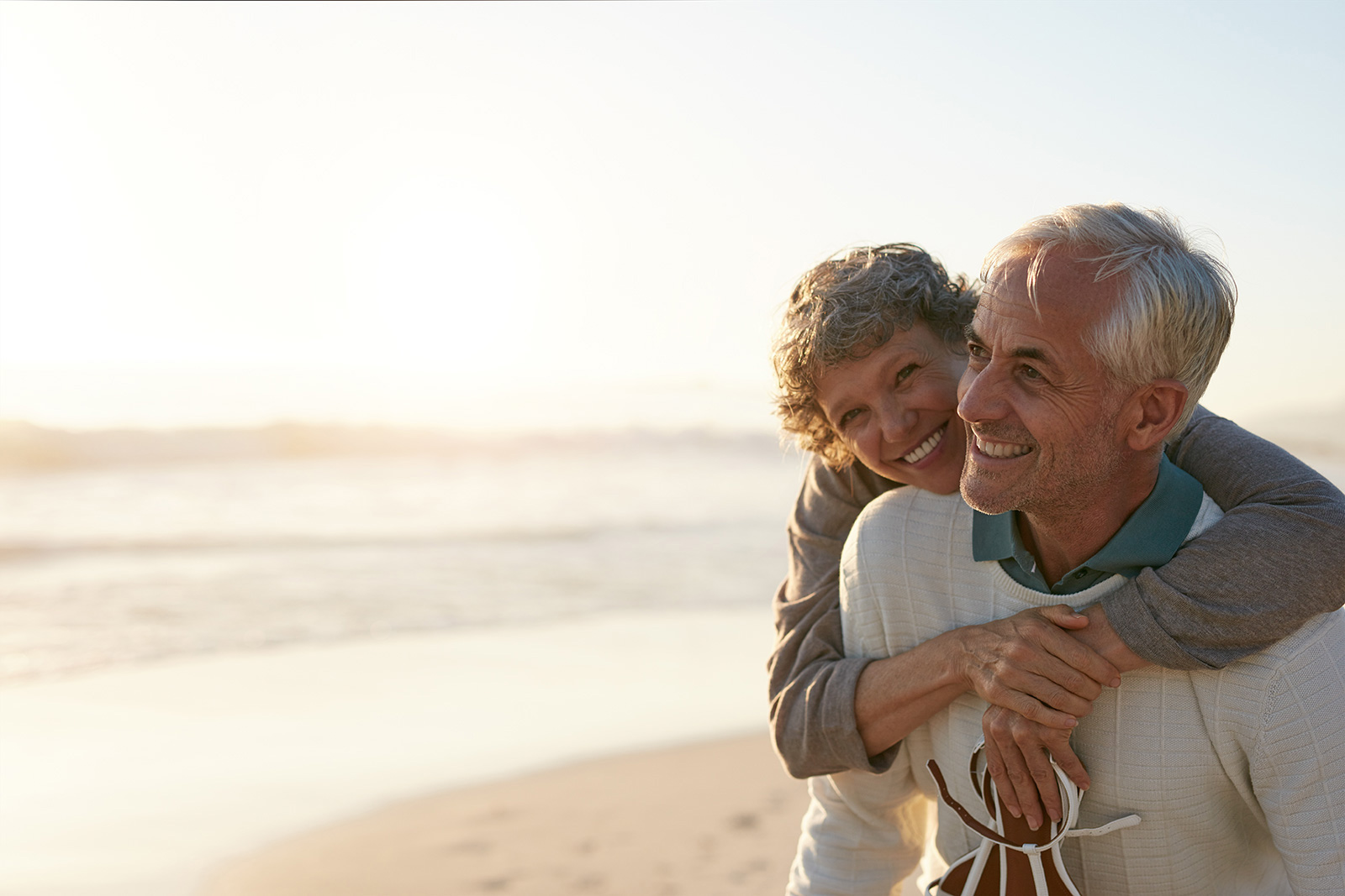 Grandfather giving granddaughter piggyback ride on sunny beach shore.