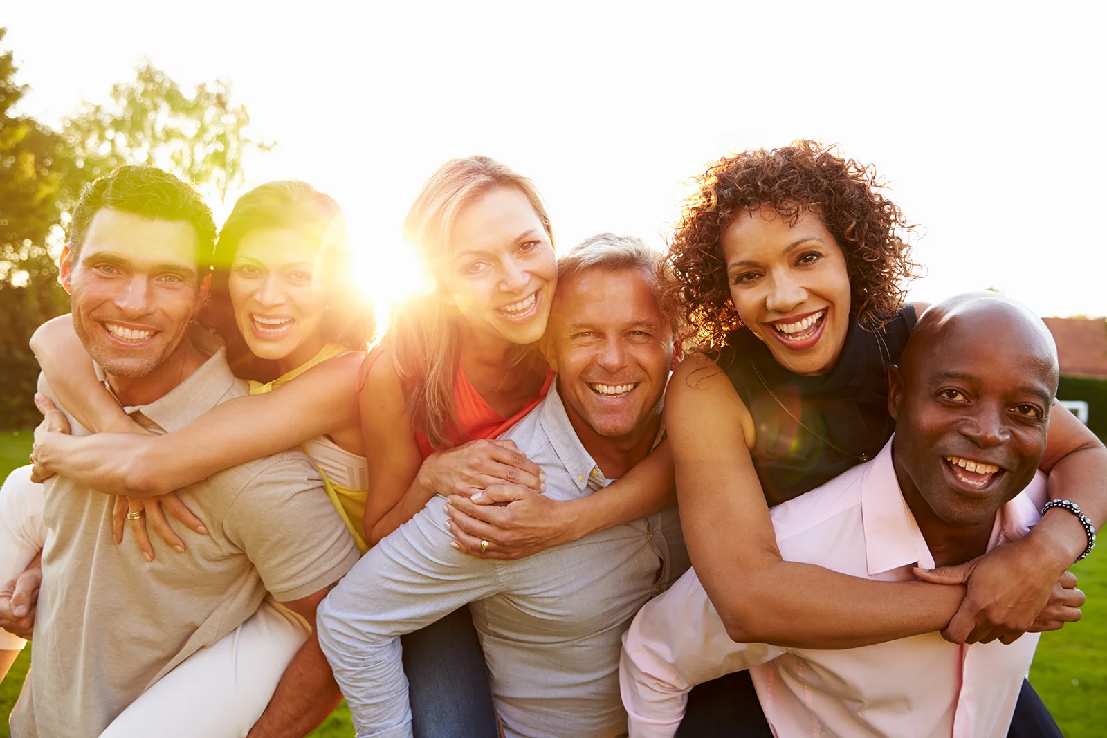 Group of smiling diverse friends hugging outdoors in sunny park setting