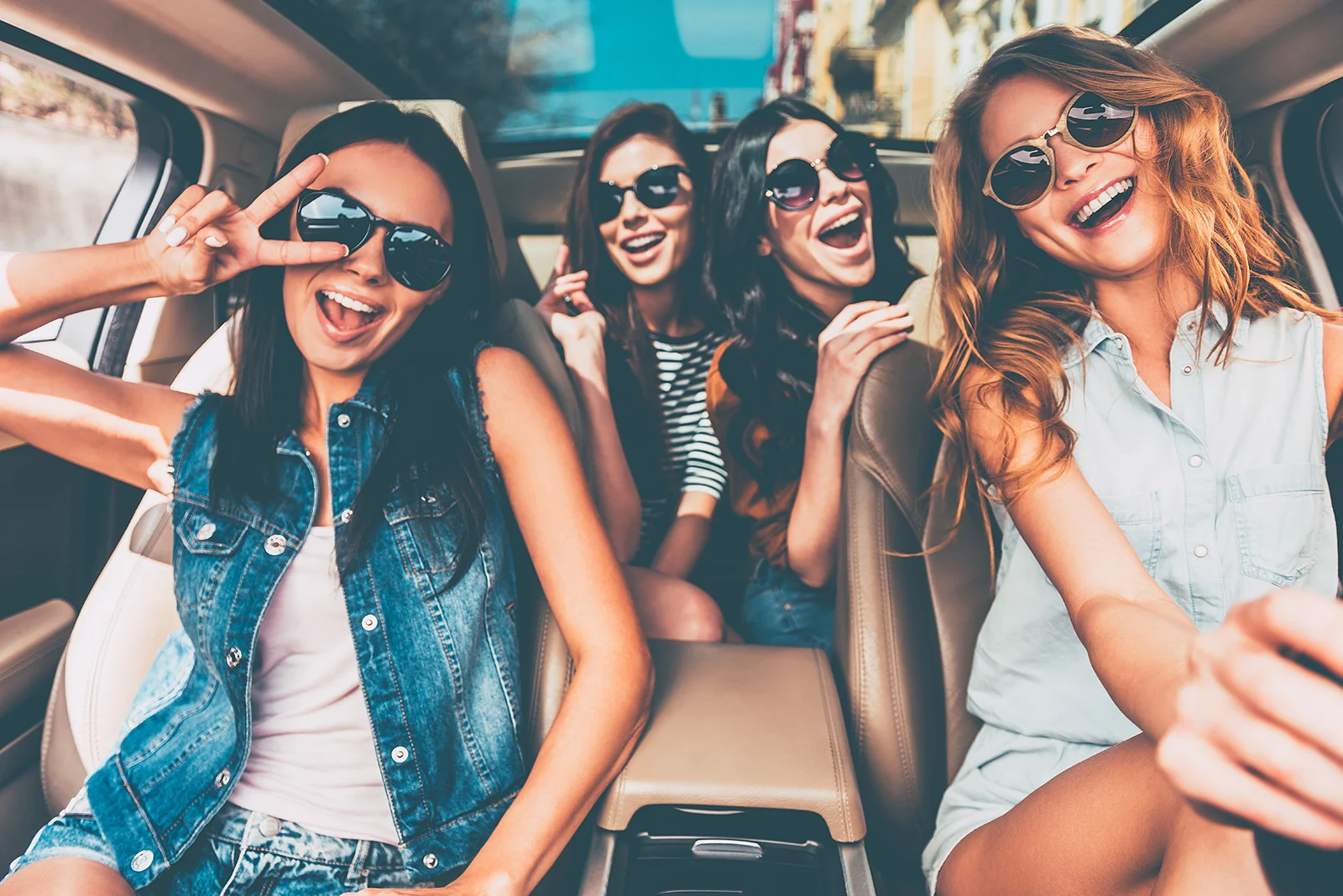 Four young women wearing sunglasses laughing together inside a vehicle.