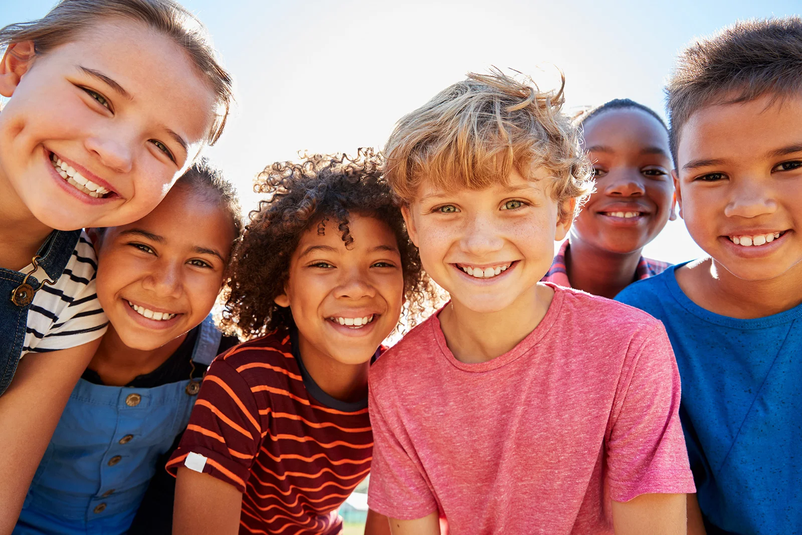 Group of smiling children outdoors in bright sunlight, looking happy and healthy.